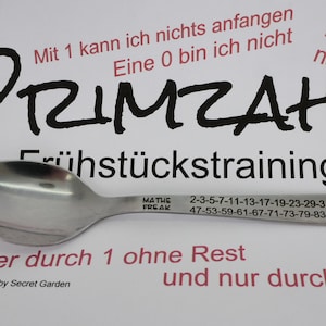 Könnte beinhalten: Ein silberner Löffel mit den Worten "Mathe Freak" und einer Liste von Primzahlen, die in den Griff graviert sind. Der Löffel liegt auf einer weißen Oberfläche mit dem Text "PRIMZAHL Frühstückstraining" und "Immer durch 1 ohne Rest und nur durch mich..." in Schwarz.