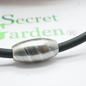 Könnte beinhalten: Ein silbernes Armband mit einer strukturierten, ovalen Perle. Das Armband ist aus schwarzem Leder.