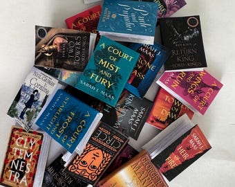 Puede incluir: Una colección de libros en miniatura con varios títulos y autores, incluyendo "Orgullo y Prejuicio", "A Court of Mist and Fury" y "El Hobbit". Los libros son de varios colores, con texto visible en las portadas.