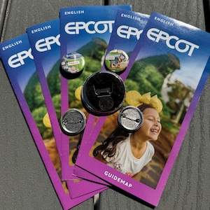 Puede incluir: Un conjunto de guías de EPCOT, pines y un abrebotellas. Las guías son moradas y azules con el logotipo de EPCOT y una niña sonriente. Los pines presentan diseños de los pabellones de Francia y China. El abrebotellas es negro.
