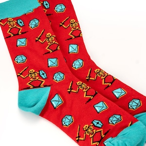May include: A pair of red socks with a turquoise cuff. The socks feature a repeating pattern of skeletons holding swords and blue diamonds.