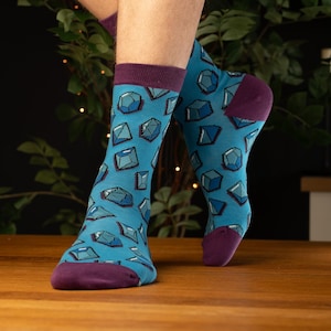 May include: A pair of blue socks with a geometric pattern of teal and purple diamonds. The socks have a purple cuff.