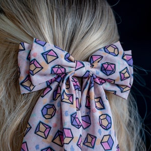 May include: A pink hair bow with a geometric pattern of colorful diamonds. The bow is tied in a large, loose knot.