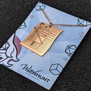 Rose gold character sheet necklace pendant displayed on branded card. Perfect D&D character sheet jewelry for tabletop RPG fans seeking unique Dungeons & Dragons accessories.