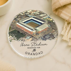 May include: A clear, round coaster featuring an aerial view of Ibrox Stadium. The coaster has the text "Ibrox Stadium RESERVED FOR GRANDAD" in black script. A soccer ball graphic is between the words "FOR" and "GRANDAD".