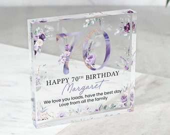 May include: A clear acrylic block with a floral design and the number 70 in purple and gold glitter. The text "HAPPY 70TH BIRTHDAY Margaret We love you loads, have the best day Love from all the family" is printed on the block.