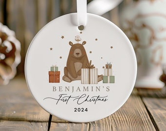 May include: White ceramic Christmas ornament with a brown bear holding a gift, a bird on top of the bear's head, and the text "Benjamin's First Christmas 2024".
