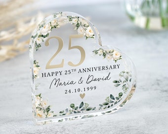 May include: A clear heart-shaped acrylic ornament with a floral design and gold lettering. The ornament says "Happy 25th Anniversary Maria & David 24.10.1999".