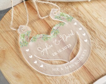 May include: Clear acrylic horseshoe wedding decoration with a heart-shaped cutout and floral design. The text "Sophie & David 28.10.2023 MR & MRS ROBERTS" is printed on the horseshoe.