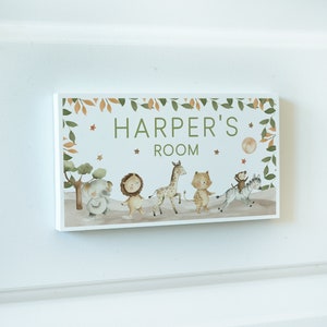 May include: A wooden sign with a green leafy border and a white background. The sign says "Harper's Room" and features a line of cartoon animals including an elephant, lion, giraffe, cat, monkey, and zebra.