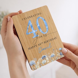 May include: A wooden birthday card with the text "Celebrating 40 Years Happy 40th Birthday David". The number 40 is in light blue with a cloud-like pattern. Floral illustrations are at the bottom.