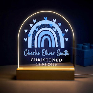 May include: An arched acrylic night light with a wooden base, featuring a blue rainbow graphic surrounded by small hearts. The text reads Charlie Oliver Smith, CHRISTENED, and 15.08.2026. The light emits a warm glow from the bottom edge of the acrylic.