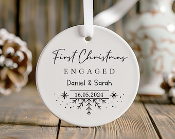 May include: White ceramic Christmas ornament with black text that reads "First Christmas Engaged Daniel & Sarah 16.05.2024" with a snowflake design.