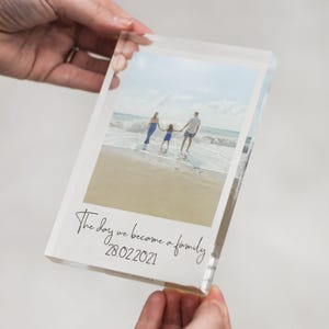 May include: A clear acrylic block displaying a family photograph taken on a beach. The image features a family of three. The text "The day we became a family 28.02.2021" is printed in black script at the bottom.