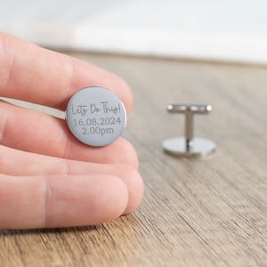 May include: Silver cufflinks with a round, engraved design. The engraving reads "Let's Do This! 16.08.2024 2.00pm".