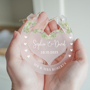 K&ouml;nnte beinhalten: Ein transparenter, hufeisenf&ouml;rmiger Anh&auml;nger aus Acryl mit einem Blumendesign und dem Text "Sophie & David 28.10.2023 MR & MRS ROBERTS" in Wei&szlig;.