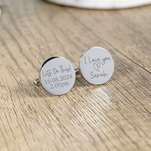 May include: A pair of silver cufflinks with engraved messages. One cufflink says "Let's Do This! 16.08.2024 2.00pm" and the other says "I Love you Sarah" with a heart symbol.