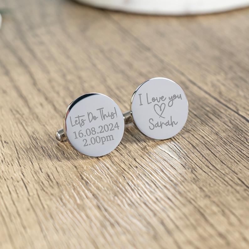 May include: A pair of silver cufflinks with engraved messages. One cufflink says "Let's Do This! 16.08.2024 2.00pm" and the other says "I Love you Sarah" with a heart symbol.