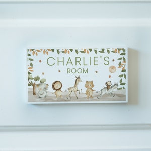 May include: A wooden sign with a green leafy border and a white background. The sign says "Charlie's Room" in green letters. There are illustrations of animals including a lion, giraffe, elephant, monkey, and zebra.