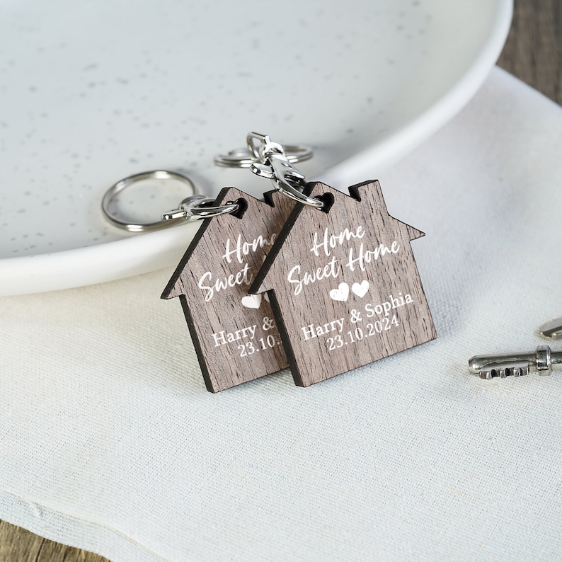 May include: Two wooden house-shaped keychains with the text "Home Sweet Home" and "Harry & Sophia 23.10.2024" on them.