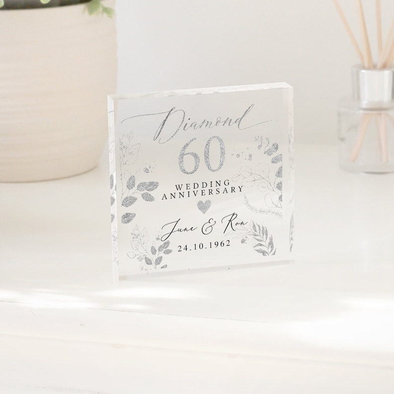 K&ouml;nnte beinhalten: Ein klarer Acrylblock mit einem silbernen Glitzerdesign. Der Block zeigt den Text "Diamond 60 Wedding Anniversary" und die Namen "June & Ron" mit dem Datum "24.10.1962".