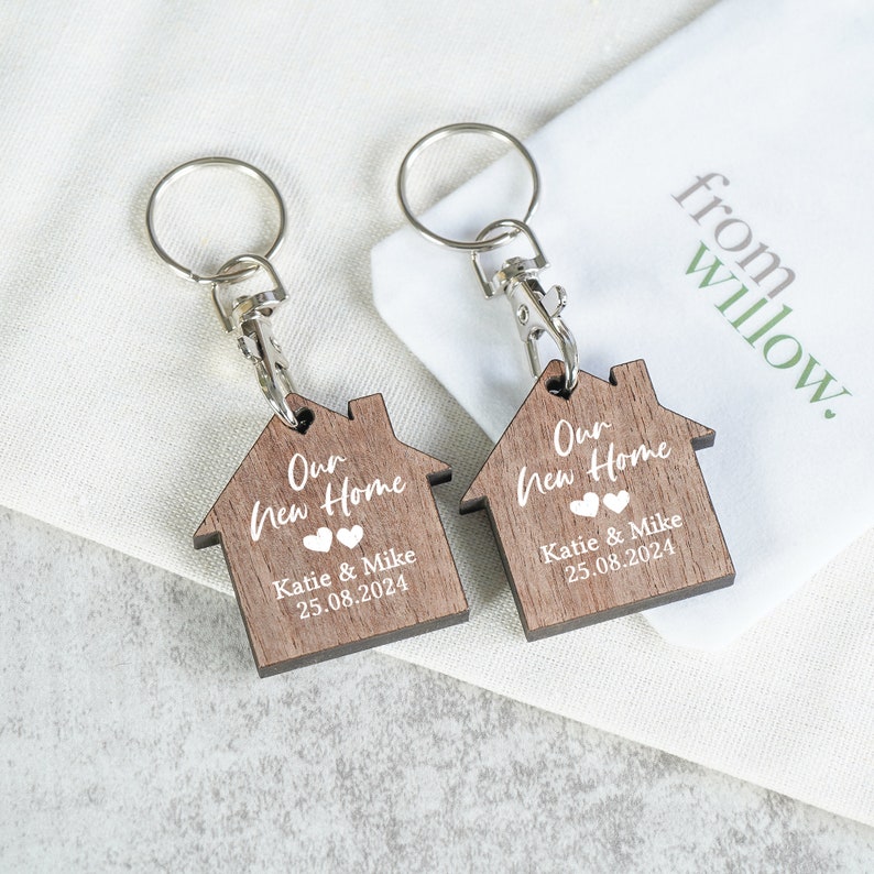 May include: Two wooden house-shaped keychains with the text "Our New Home" and the names "Katie & Mike" and the date "25.08.2024".