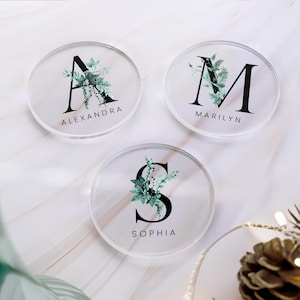 May include: Three clear acrylic coasters with a floral design and a black letter initial in the centre. The coasters are labelled "Alexandra", "Marilyn", and "Sophia".