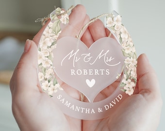 May include: A white acrylic horseshoe with a floral design and a heart-shaped cutout. The heart has the text "Mr & Mrs ROBERTS" and a small heart. The bottom of the horseshoe has the text "SAMANTHA & DAVID".