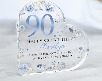May include: A heart-shaped acrylic keepsake with the number "90" in light blue. The text reads "HAPPY 90TH BIRTHDAY Marilyn" with a floral design. The bottom of the keepsake says "Have the best day on your 90th! We love you so very much x."