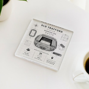 May include: A square glass coaster featuring a black and white architectural blueprint design of Old Trafford stadium. The print includes the text Old Trafford Stadium, Reserved for David, capacity 74,197, opened 1910, and coordinates 53°27'47.0"N 2°17'28.8"W.