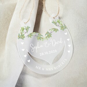 K&ouml;nnte beinhalten: Wei&szlig;e hufeisenf&ouml;rmige Acryl-Hochzeitsdekoration mit gr&uuml;nem Blumendesign und dem Text "Sophie & David" und "28.10.2023". Der untere Teil des Hufeisens tr&auml;gt die Aufschrift "Mr & Mrs Roberts".