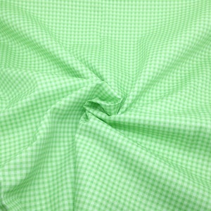 May include: A green and white gingham fabric with a checkered pattern. The fabric is folded and wrinkled, creating a textured look.