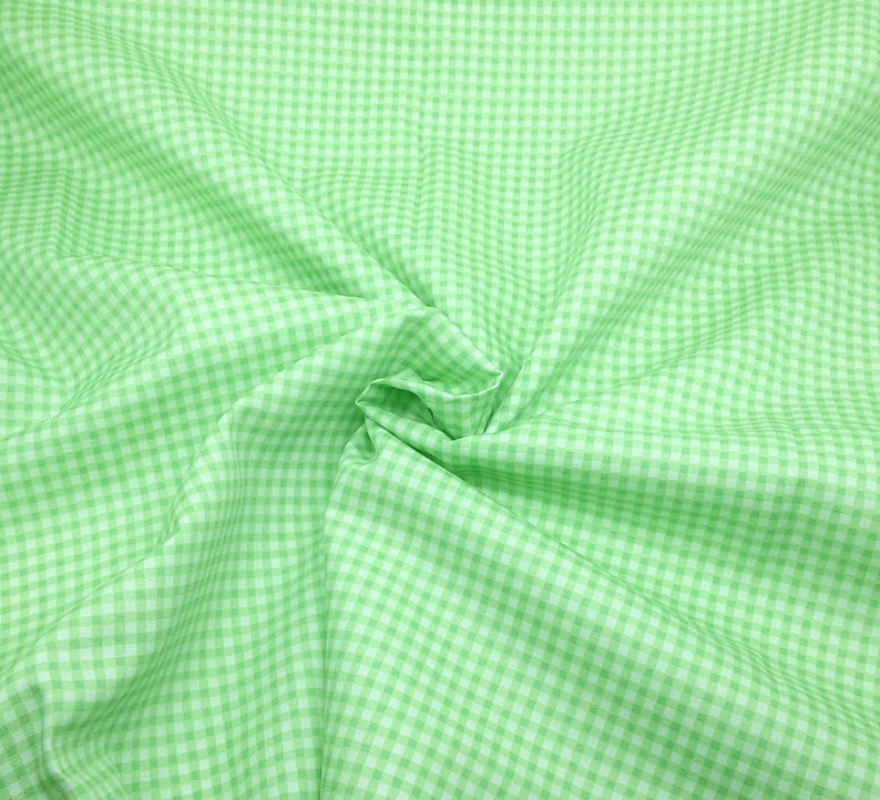 May include: A green and white gingham fabric with a checkered pattern. The fabric is folded and wrinkled, creating a textured look.