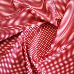 May include: Red and white gingham fabric with a checkered pattern. The fabric is folded and draped, creating a soft, textured look.
