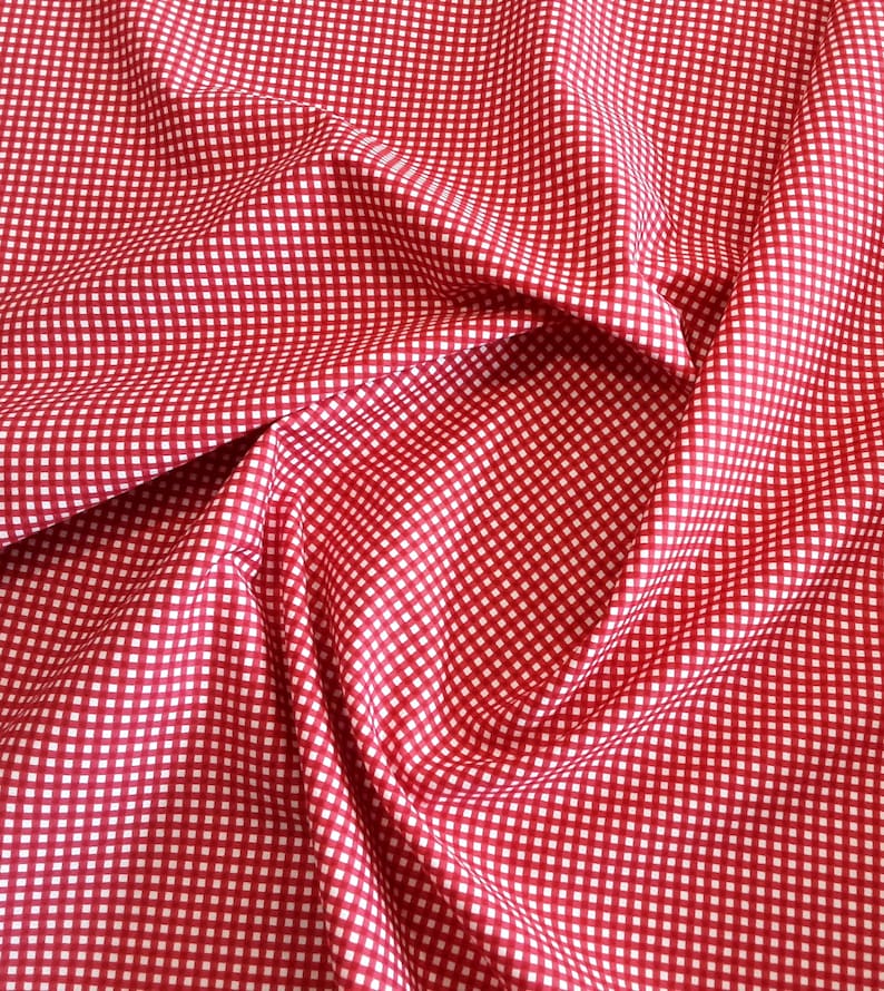 May include: Red and white gingham fabric with a checkered pattern. The fabric is folded and draped, creating a soft, textured look.