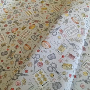 May include: A pale fabric printed with a sewing-themed design. The pattern includes illustrations of scissors, thread spools, pin cushions, buttons, and thimbles in grey, yellow, orange, and pink. The fabric is likely cotton or a similar material.