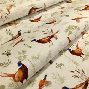 May include: Off-white fabric with a repeating pheasant design. The birds are depicted in shades of brown, orange, and blue, amidst green foliage and reeds. The fabric is likely made of cotton or linen, suitable for various textile projects.