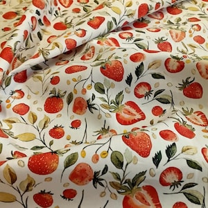 May include: White fabric featuring a repeating pattern of red strawberries, green leaves, and small yellow berries. The strawberries are whole or sliced, creating a fresh design. The fabric is likely cotton or linen, ideal for summer projects.