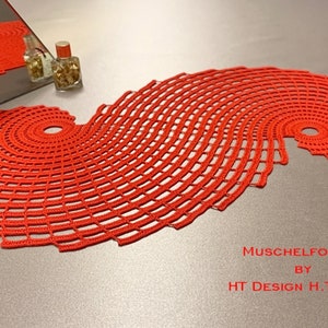 Może przedstawiać: Czerwony, szydełkowy bieżnik stołowy z wzorem spiralnym. Bieżnik nazywa się "Muschelform A" autorstwa HT Design H. Toprak.