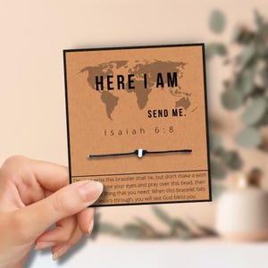 May include: A brown card with a world map graphic and the text "HERE I AM SEND ME. Isaiah 6:8." A black string bracelet with a white bead is attached. The card includes instructions.