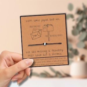 May include: A friendship bracelet on a card with the text "We are making a friendship that could last a lifetime." The card has illustrations of a mailbox and envelopes. The bracelet is black with a white bead.