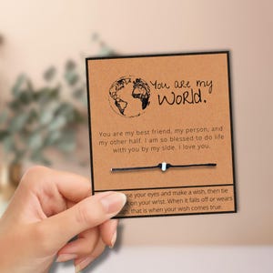 May include: A white ceramic mug with a black handle and the text "But First, Coffee" in a black, handwritten-style font. The mug is on a white surface.