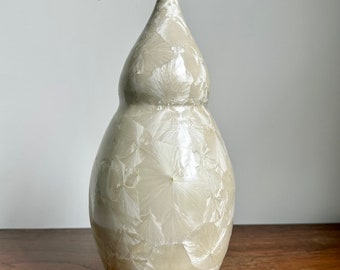 May include: A white ceramic vase with a unique, textured surface. The vase has a rounded, gourd-like shape with a long, curved neck.