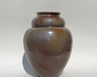 May include: A brown ceramic vase with a speckled glaze. The vase has a rounded body and a wide mouth.