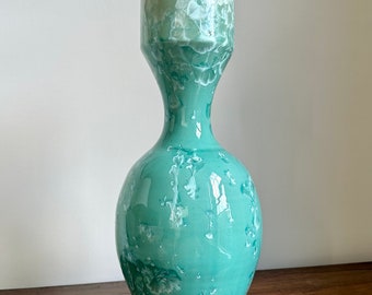 May include: A light green ceramic vase with a white marbled design. The vase has a wide mouth and a narrow base.