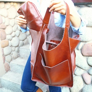 Puede incluir: Un bolso tote grande de cuero marr&oacute;n con un bolsillo con cremallera y una bolsa de cuero marr&oacute;n m&aacute;s peque&ntilde;a en el interior. El bolso tiene una correa larga y se lleva sobre el hombro.