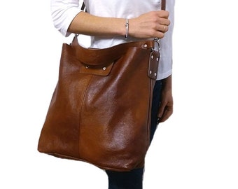 Puede incluir: Un bolso tote de cuero marrón con una correa larga. El bolso tiene una cremallera y una solapa con un cierre de presión.