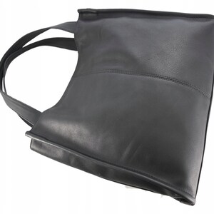 May include: Black leather tote bag with a rectangular shape and a single shoulder strap. The bag features a stitched horizontal seam across the middle and a smooth, matte finish. The strap is thin and made of the same material as the bag.
