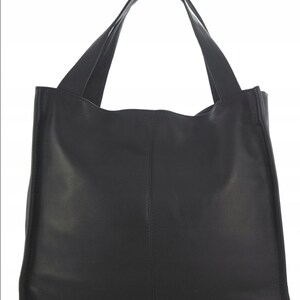 May include: A black tote bag with two long handles. The bag is made of a smooth, solid material and has a rectangular shape with a slightly curved top edge. The handles are attached to the top of the bag and are wide enough to be carried over the shoulder.