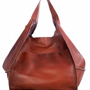 Puede incluir: Un bolso tote de cuero marr&oacute;n con un solo asa superior. El bolso tiene una parte superior grande y abierta y un solo bolsillo en la parte delantera.